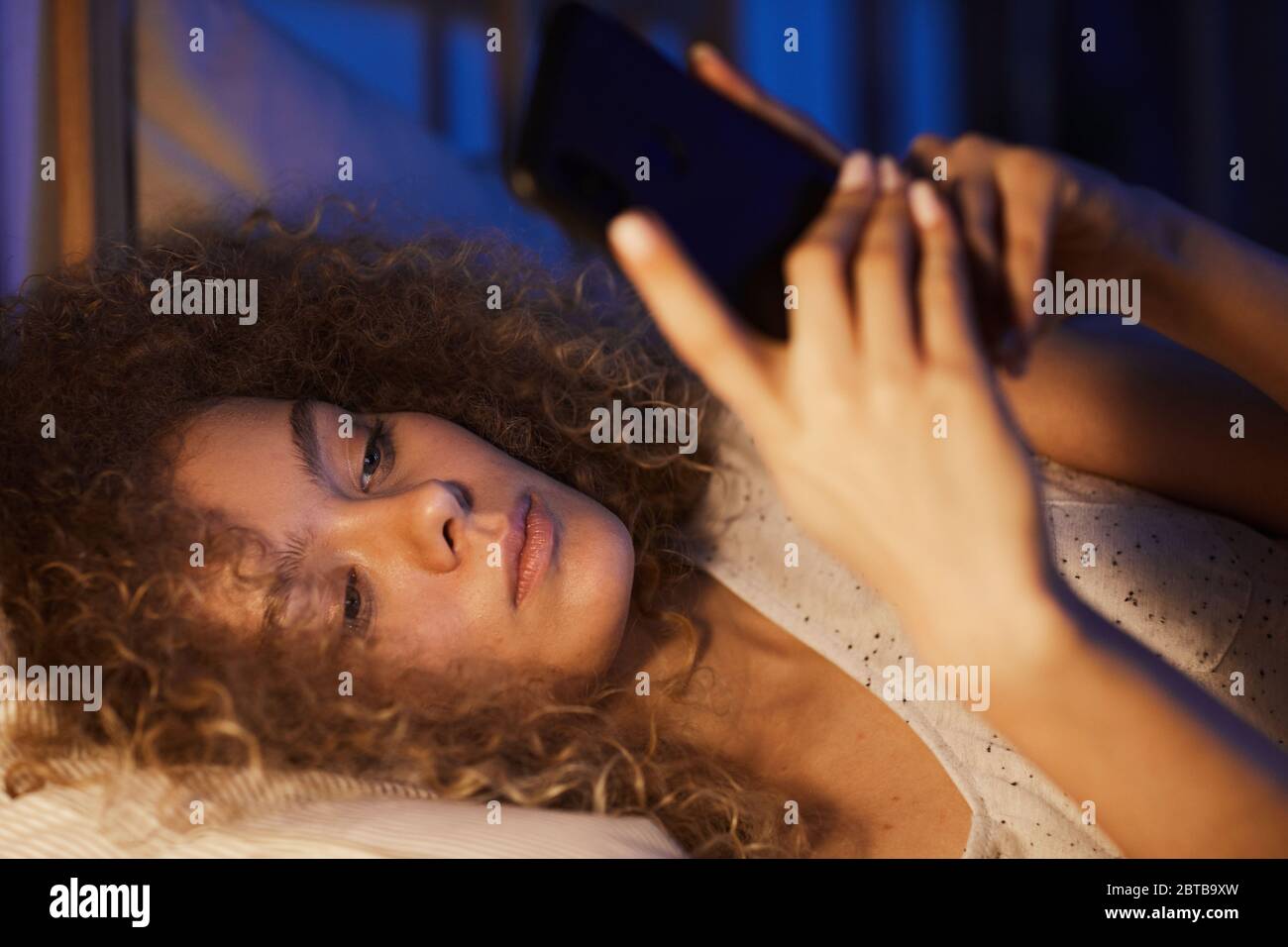 Gros plan d'une jeune femme aux cheveux bouclés, au lit la nuit, éclairée par une lumière chaleureuse et un espace de copie Banque D'Images