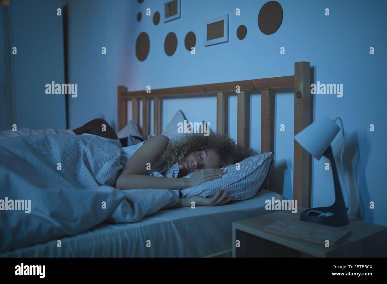 Portrait de la jeune femme aux cheveux bouclés dormant calmement dans un lit confortable la nuit, espace de copie Banque D'Images