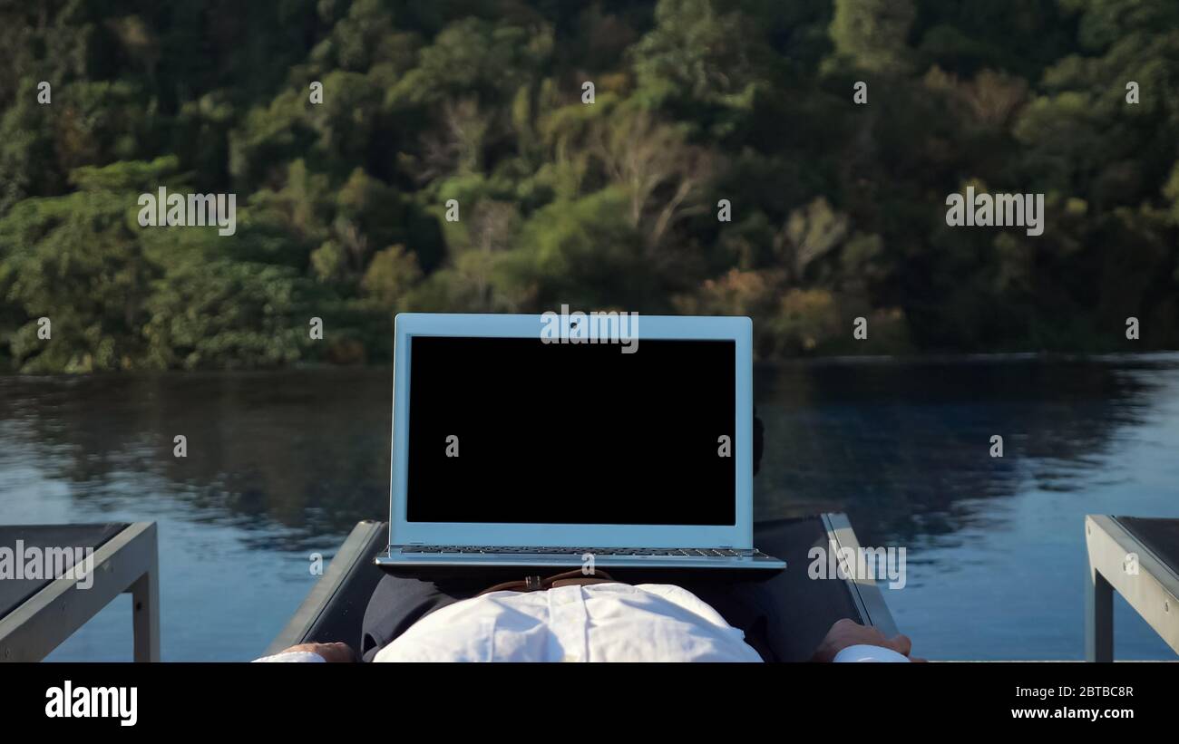 ordinateur portable avec écran sombre sur les jambes de détente dans chaise  de salon homme contre vert forêt colline jetant l'ombre sur la piscine  bleue Photo Stock - Alamy