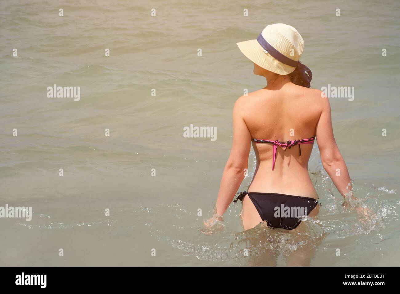 jeune jolie femme en bikini et chapeau se tient dans la mer par temps ensoleillé Banque D'Images