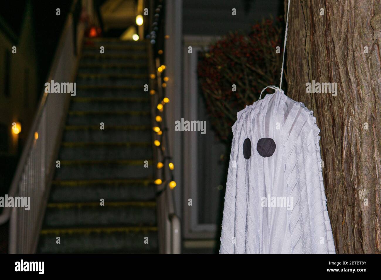 Fantôme blanc suspendu sur un arbre pendant une période de vacances pour Halloween sur fond sombre. Banque D'Images