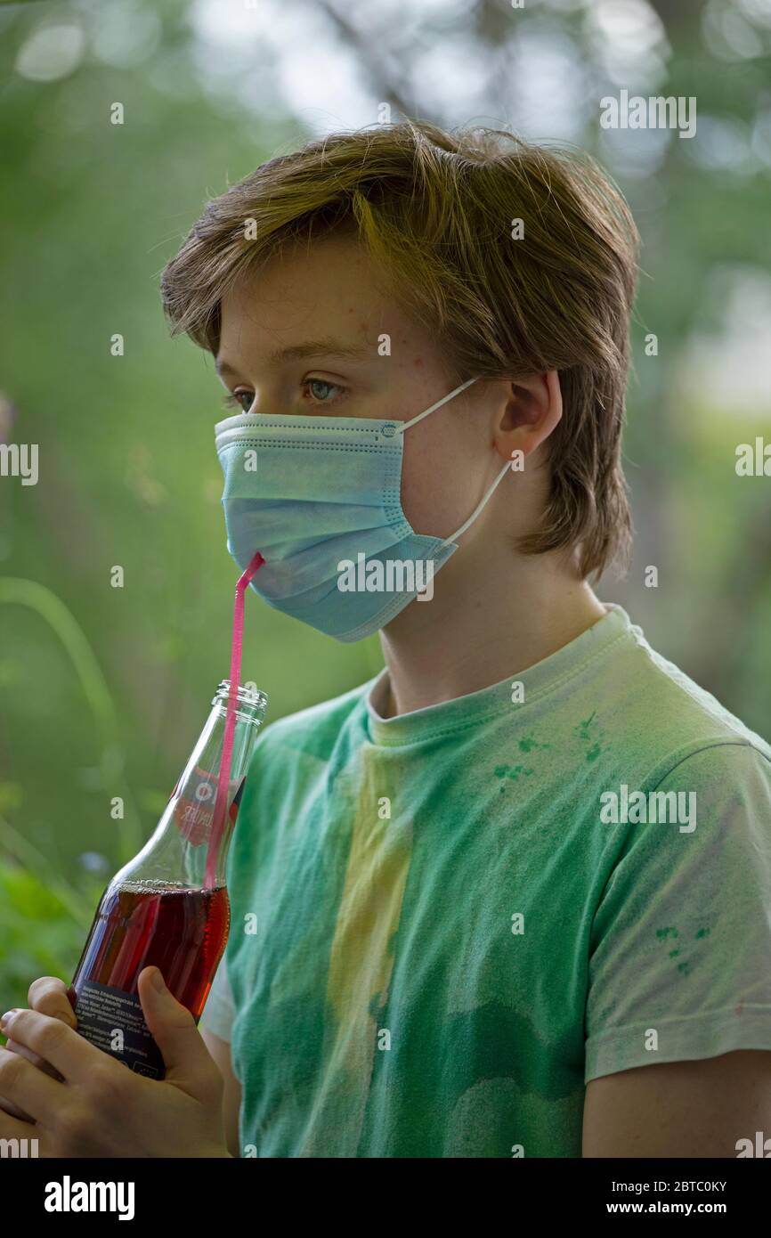 Garçon portant un masque respiratoire buvant dans une bouteille avec une paille, Allemagne Banque D'Images