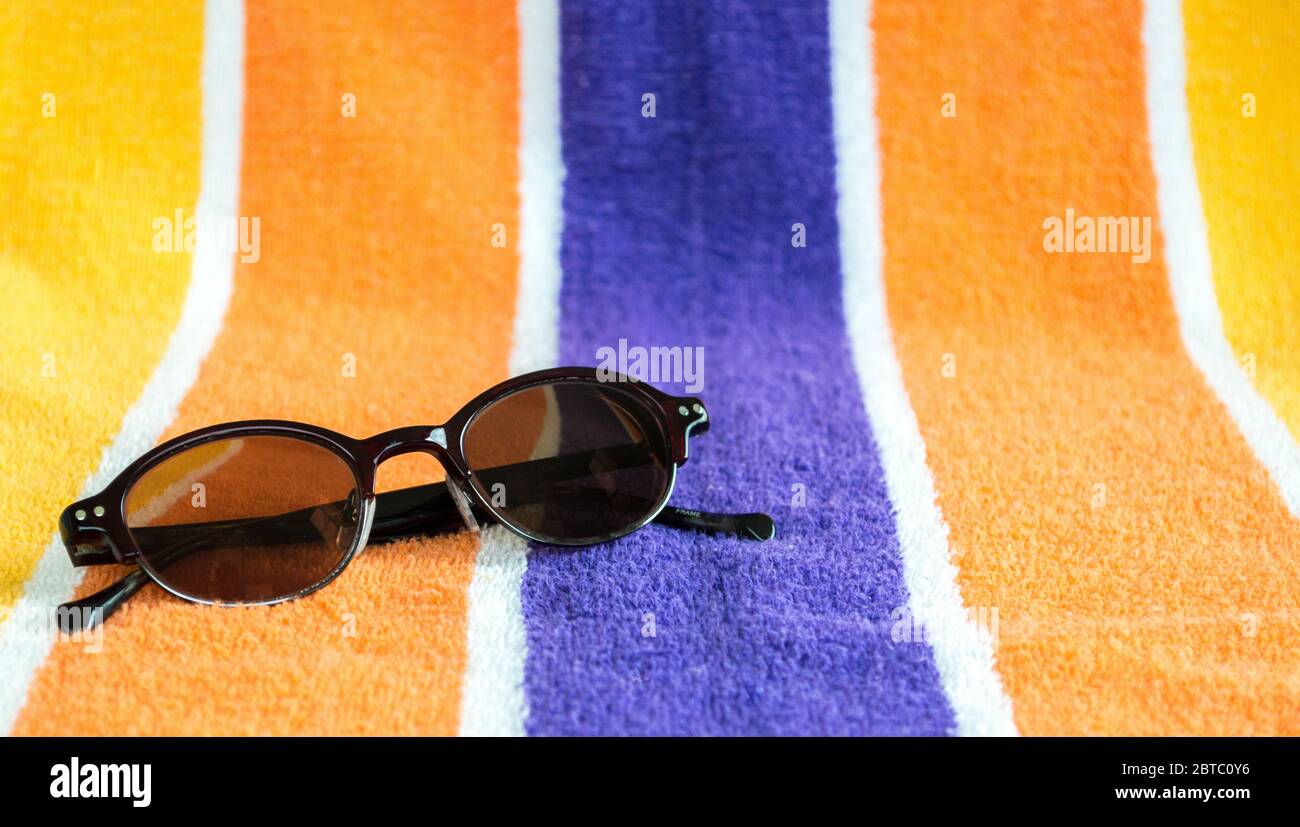 une paire de lunettes de soleil aux rayures vives, sur une serviette de plage avec espace pour copier Banque D'Images