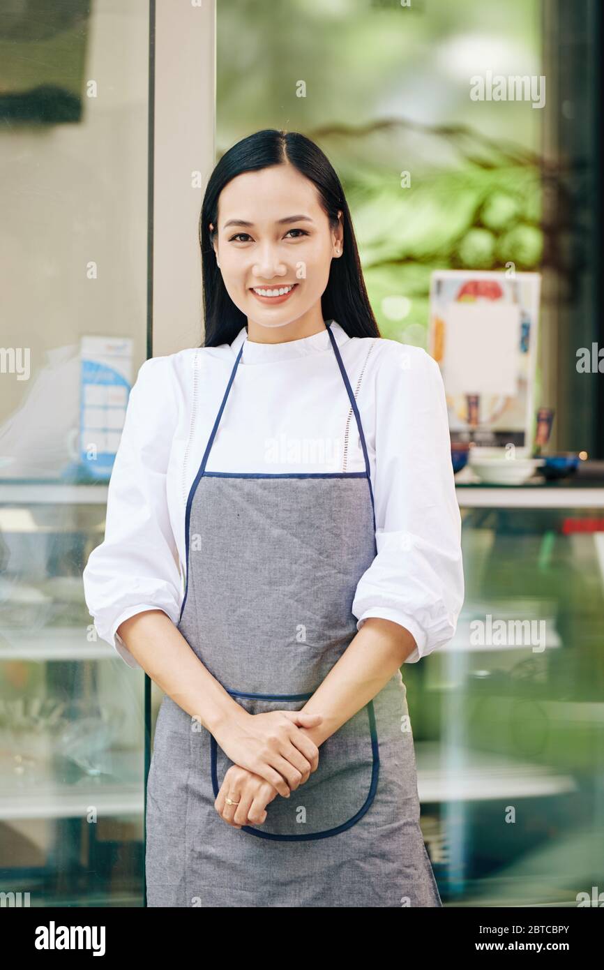 Portrait du jeune barista asiatique charmant en tablier devant le coffee eshop Banque D'Images