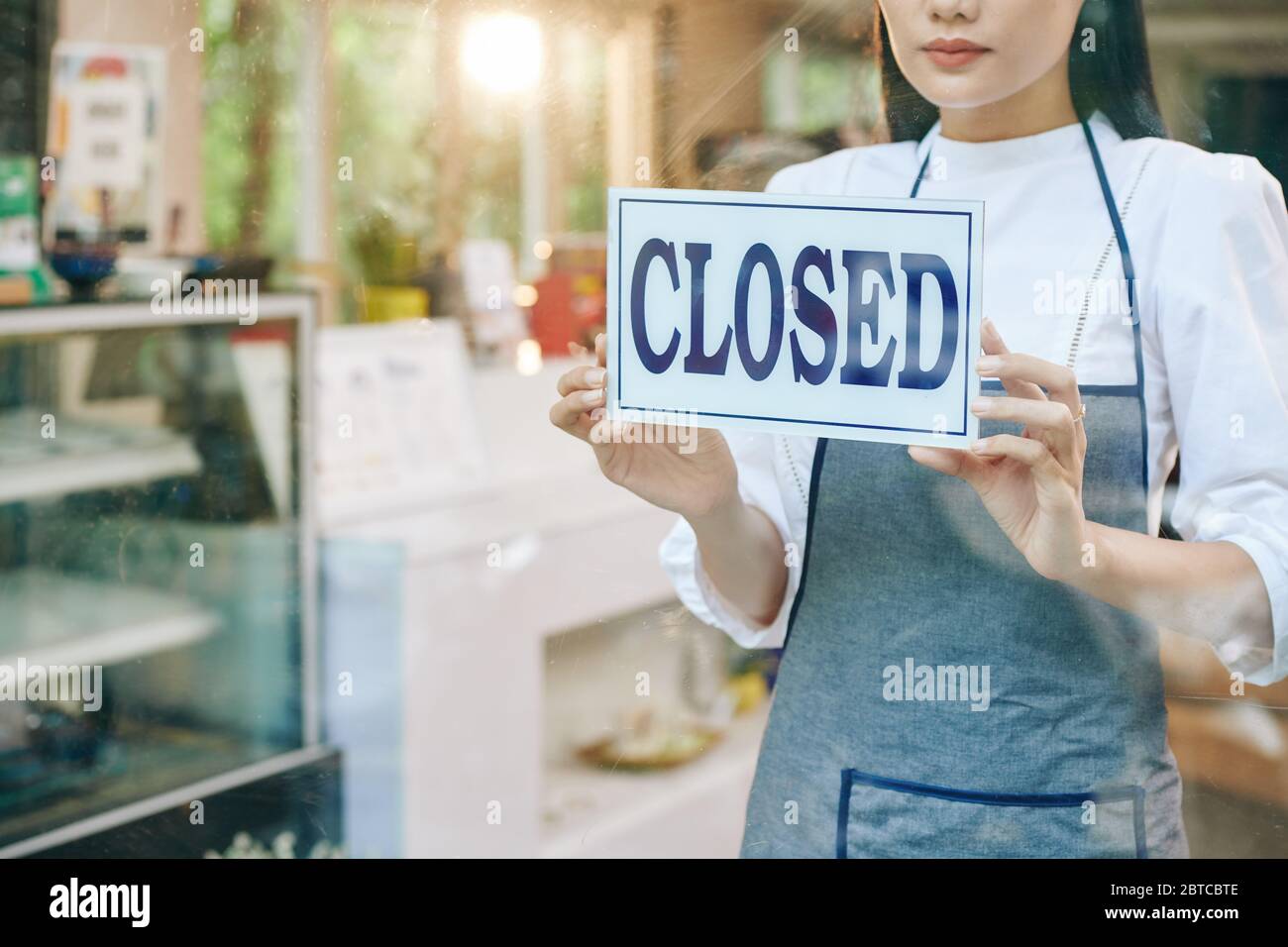 Triste femme propriétaire du restaurant fermant la porte et l'affiche suspendue Banque D'Images