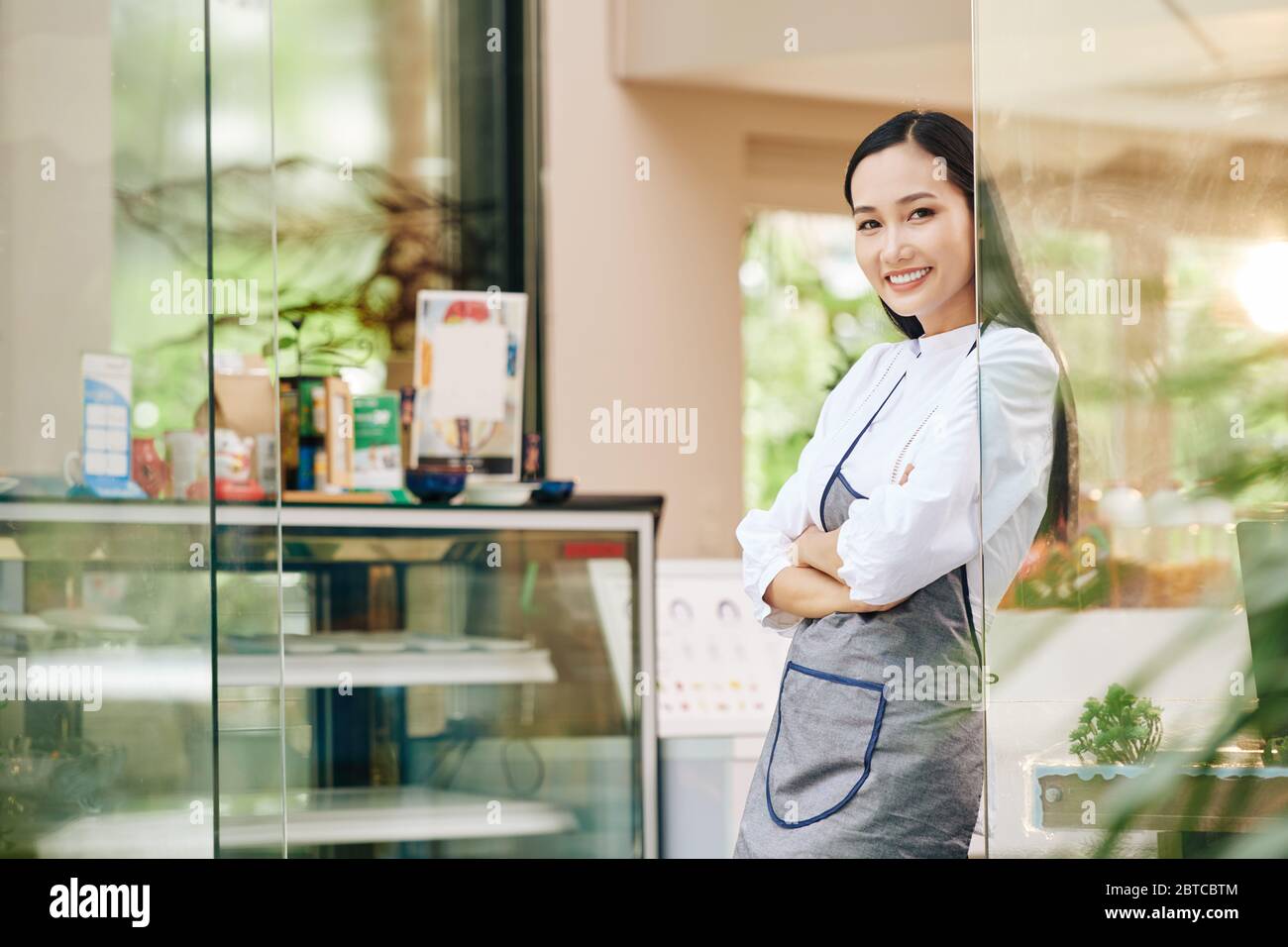 Belle serveuse jeune de café debout à l'entrée du café et souriant à la caméra Banque D'Images