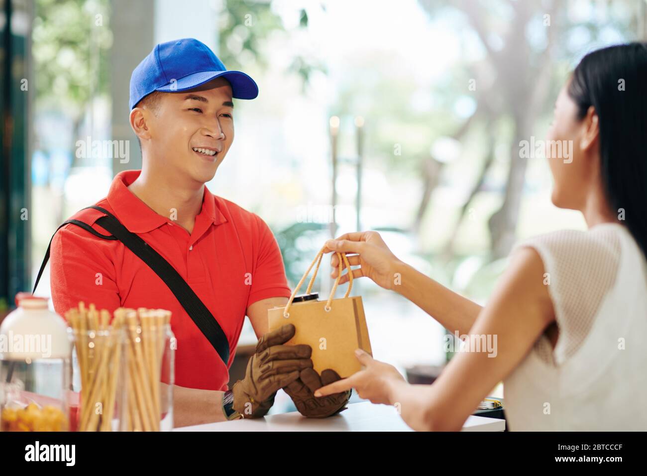 Coursier souriant en uniforme prenant la commande emballée des mains de la serveuse du café Banque D'Images