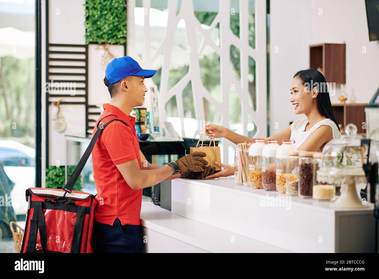 Jeune employé de café joyeux donnant la commande de clients emballés au service de messagerie Banque D'Images