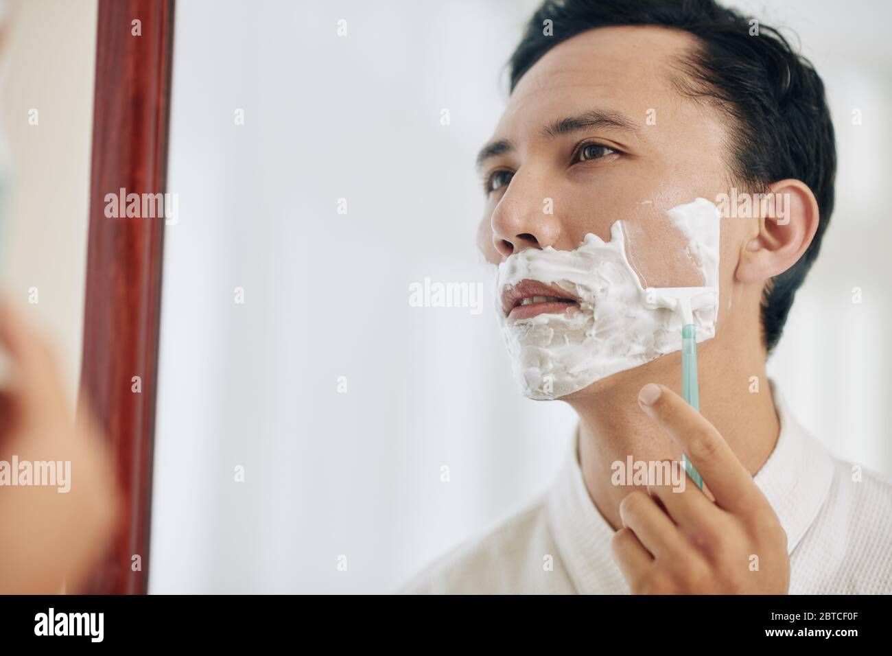Homme de course mixte se rasant devant le miroir après avoir pris une douche le matin Banque D'Images