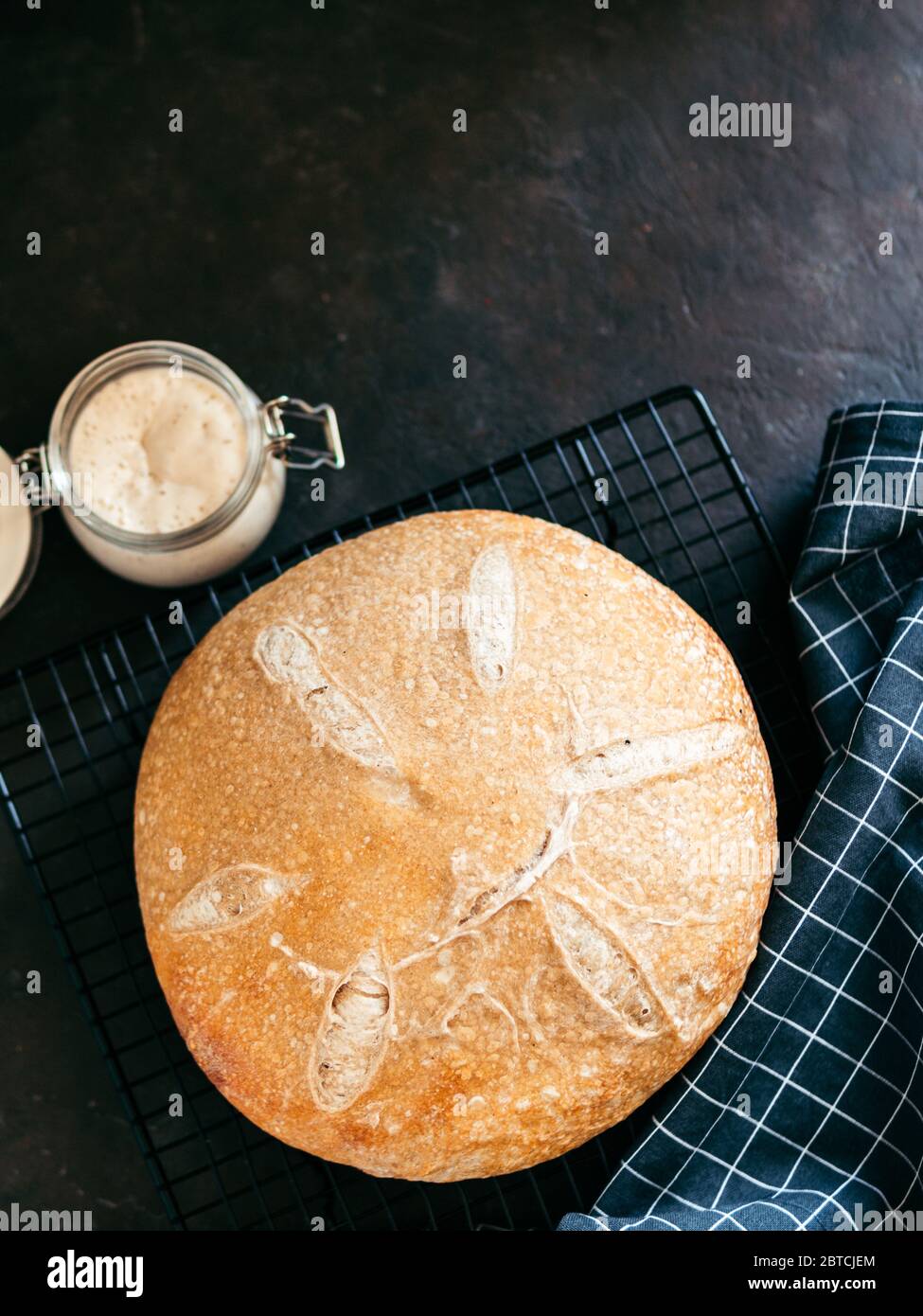 Pain au levain rond de blé et entrée de levain dans un pot en verre. Vue de dessus de délicieux pain de levain maison sur fond noir avec espace de copie. Concept de fabrication de pain au levain fait maison. Verticale. Banque D'Images