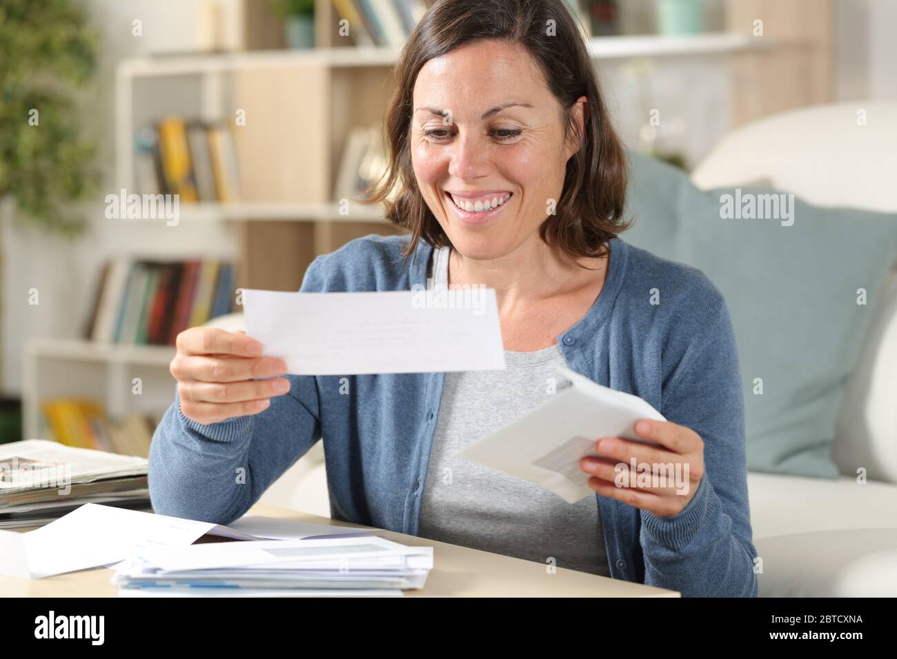 Bonne femme d'âge moyen ouvrant les lettres de reçus assis dans le salon à la maison Banque D'Images