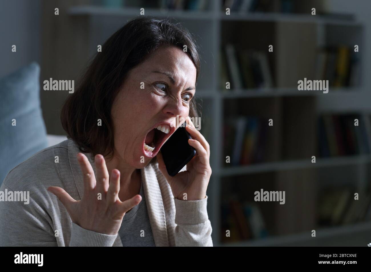 Une femme adulte en colère criait à appeler sur un smartphone assis dans le salon la nuit à la maison Banque D'Images