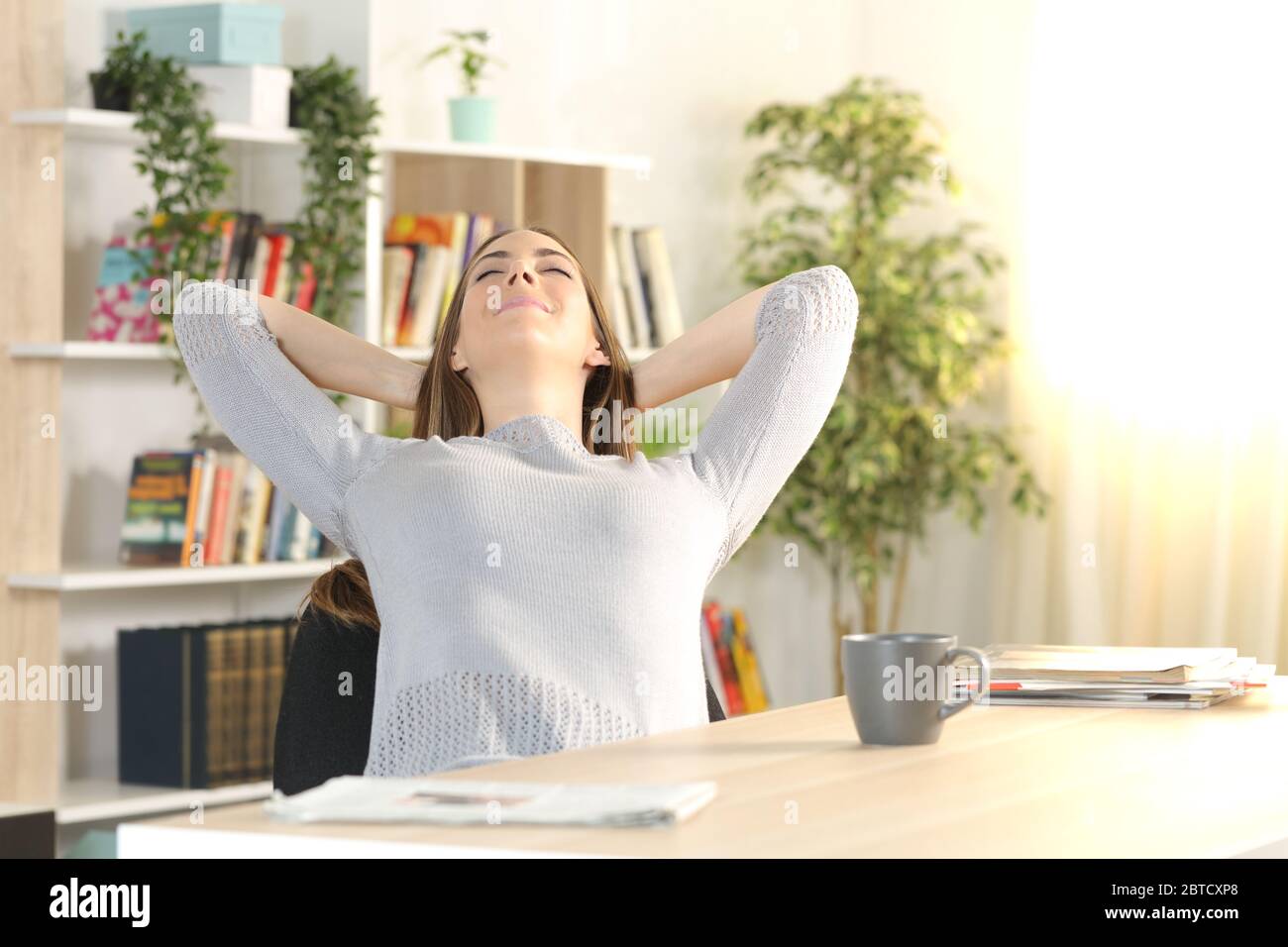 Femme satisfaite se reposant sur un bureau dans le salon à la maison Banque D'Images