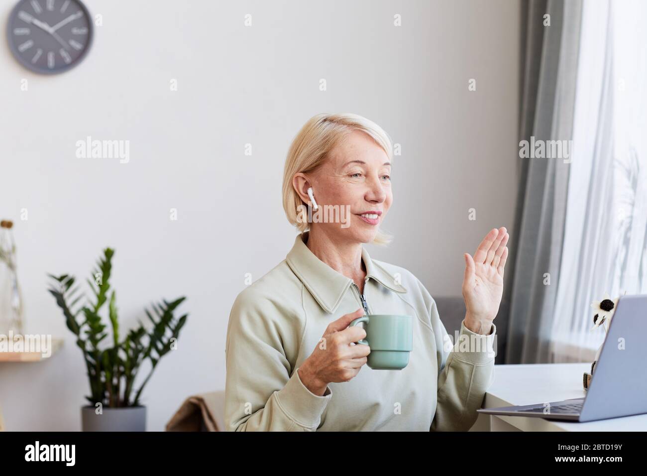 Femme mûre avec des cheveux blonds boire du café et communiquer en ligne en utilisant son ordinateur portable à la maison Banque D'Images