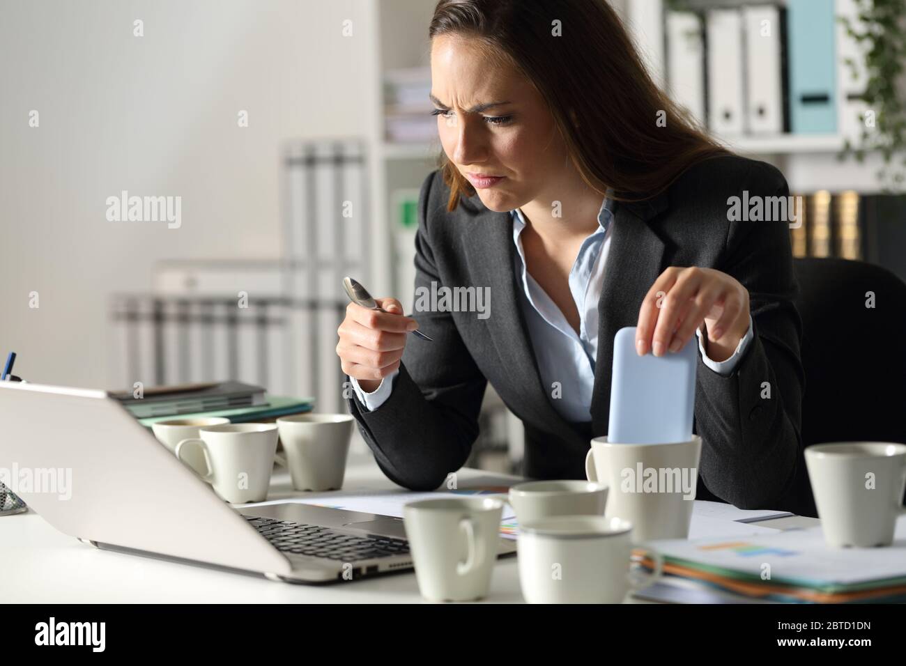 Une femme exécutive surtravaillée fait des erreurs en raison de l'épuisement avec plusieurs tasses de café assis dans la nuit au bureau Banque D'Images