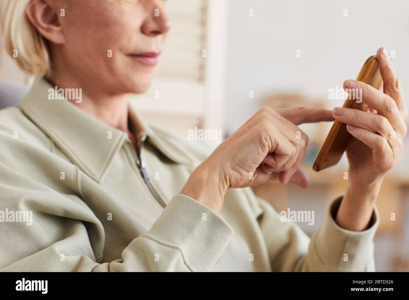 Gros plan d'une femme âgée aux cheveux blonds courts tenant un téléphone portable et en tapant un message Banque D'Images