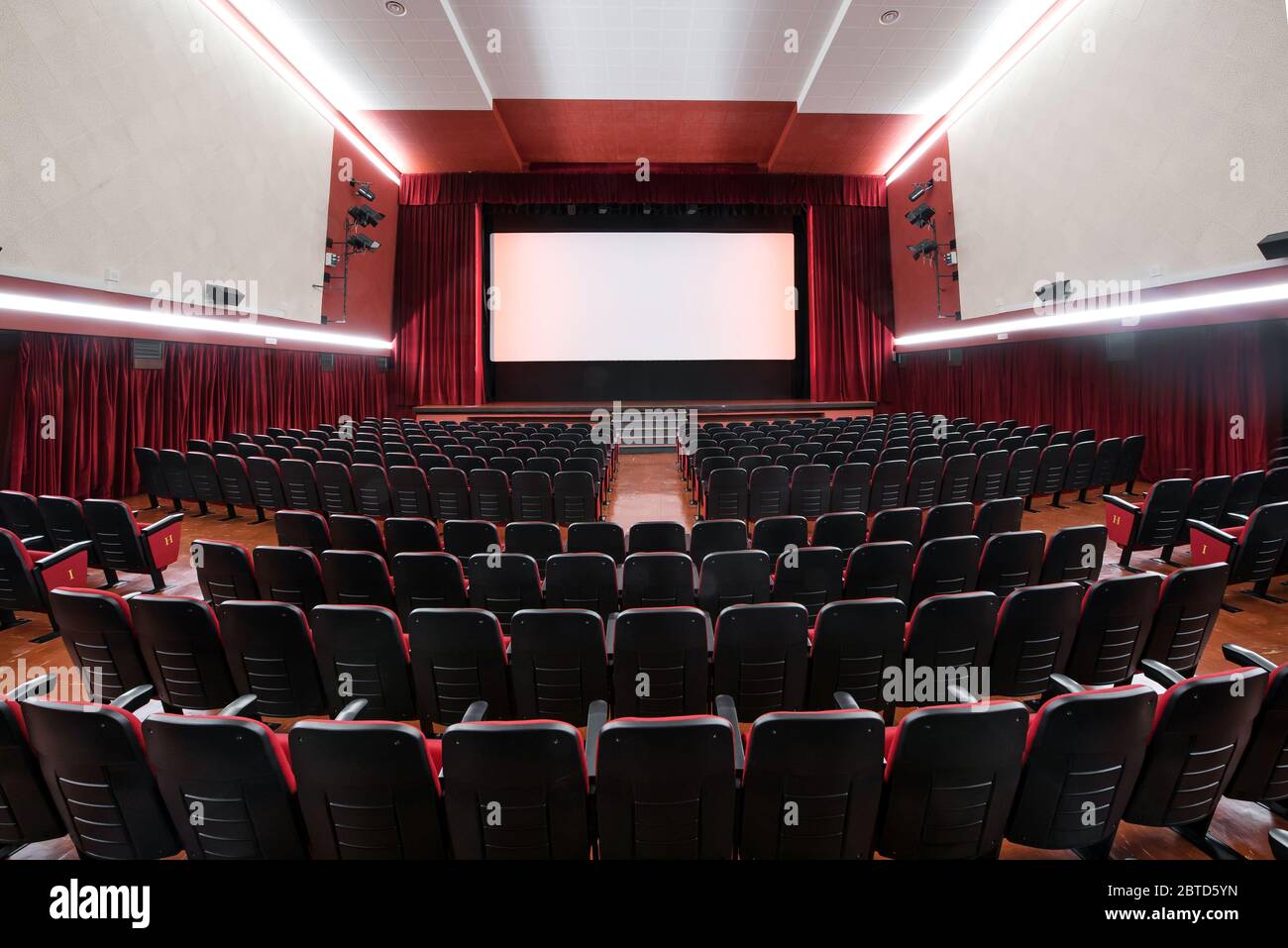 Vue panoramique de l'intérieur d'un cinéma montrant l'architecture et les rangées de sièges rouges vides surplombant une scène déserte Banque D'Images