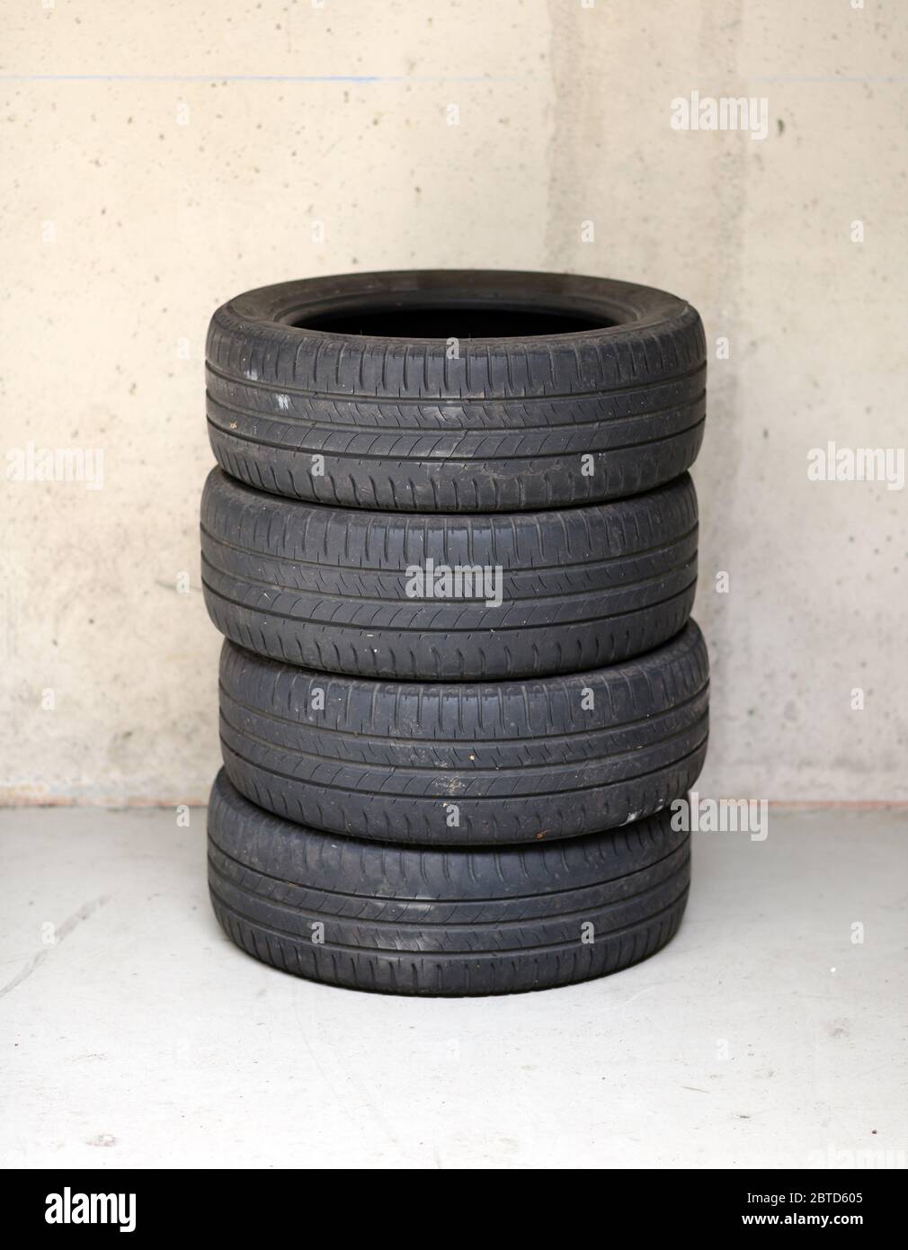Ensemble de quatre pneus empilés pour voitures d'occasion ou véhicules automobiles sur un sol en béton contre un mur avec espace de copie Banque D'Images
