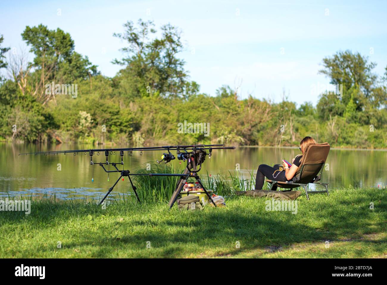Jeune femme assise près du lac avec du matériel de pêche Banque D'Images