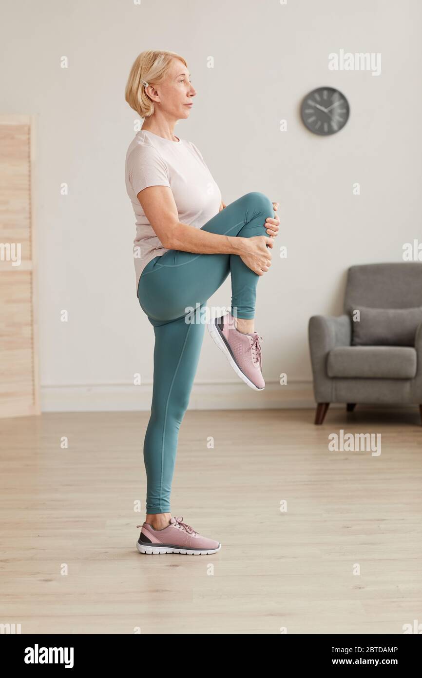 Femme mature debout et étirant sa jambe pendant les exercices à la maison Banque D'Images