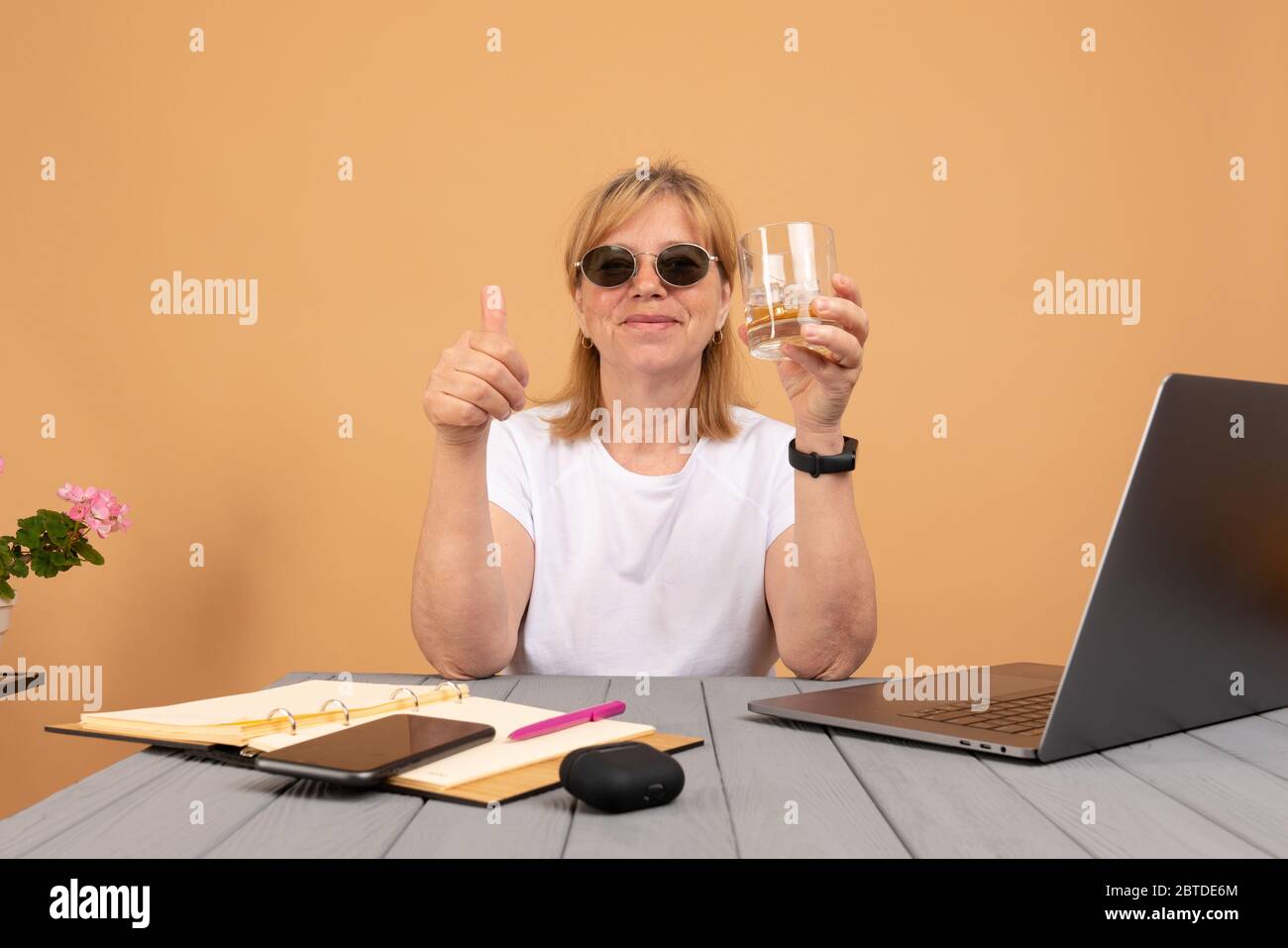 Bonne femme âgée ivre en lunettes de soleil, buvant du whisky et travaillant sur son ordinateur Banque D'Images