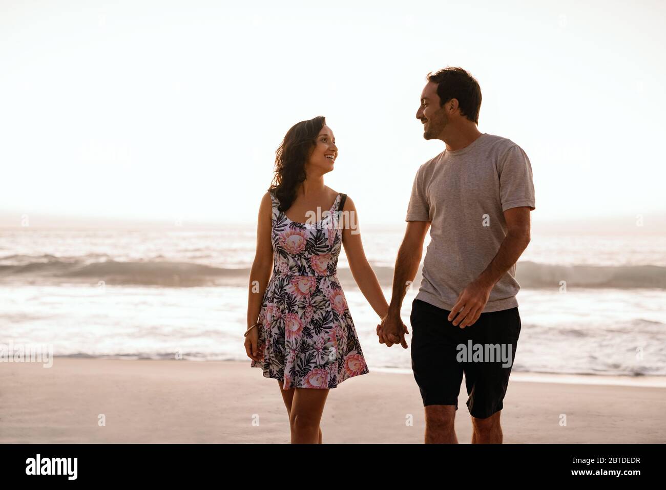 Un jeune couple tient les mains et marche le long d'une plage de sable Banque D'Images