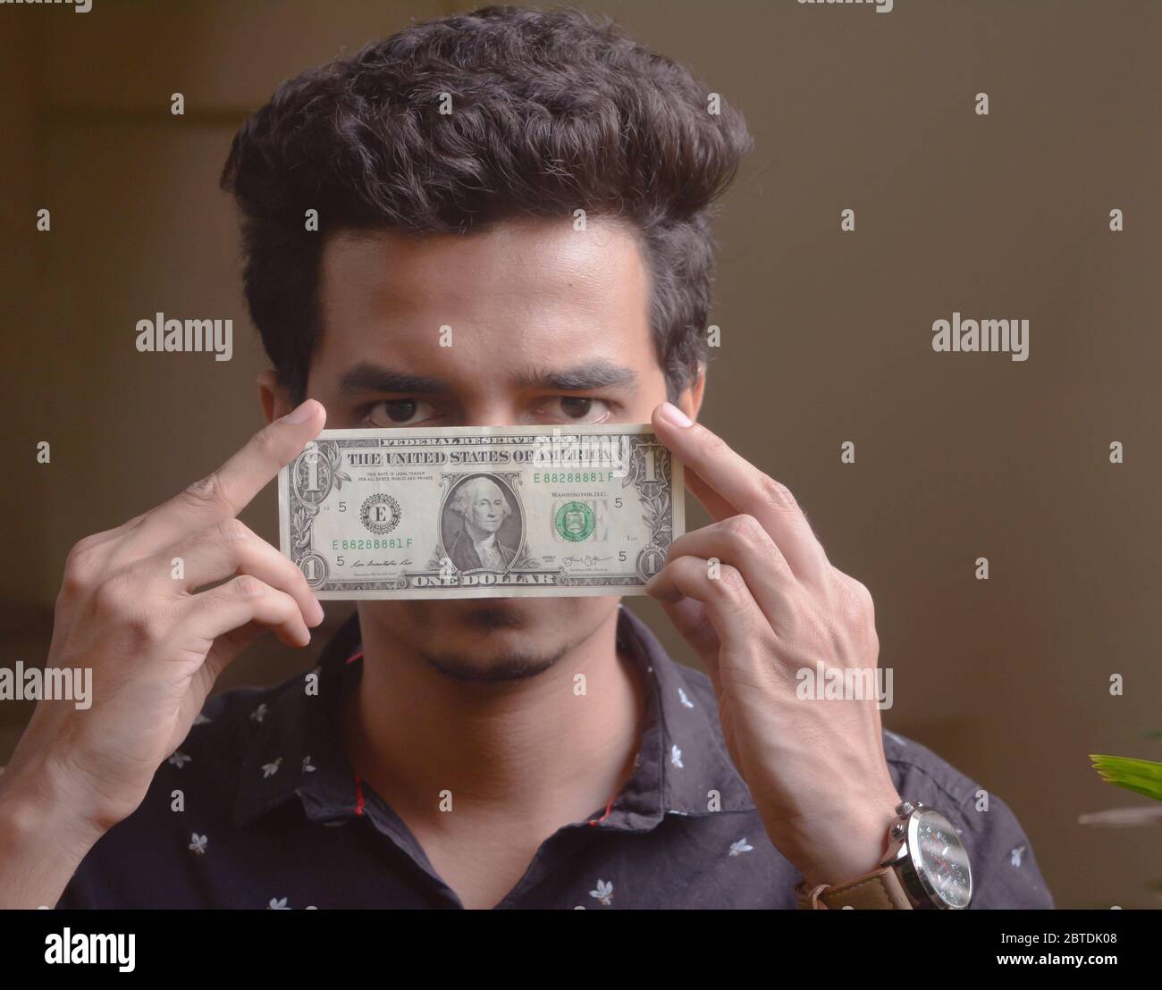 Le jeune homme tient le billet de dollar devant son visage . un dollar. Banque D'Images