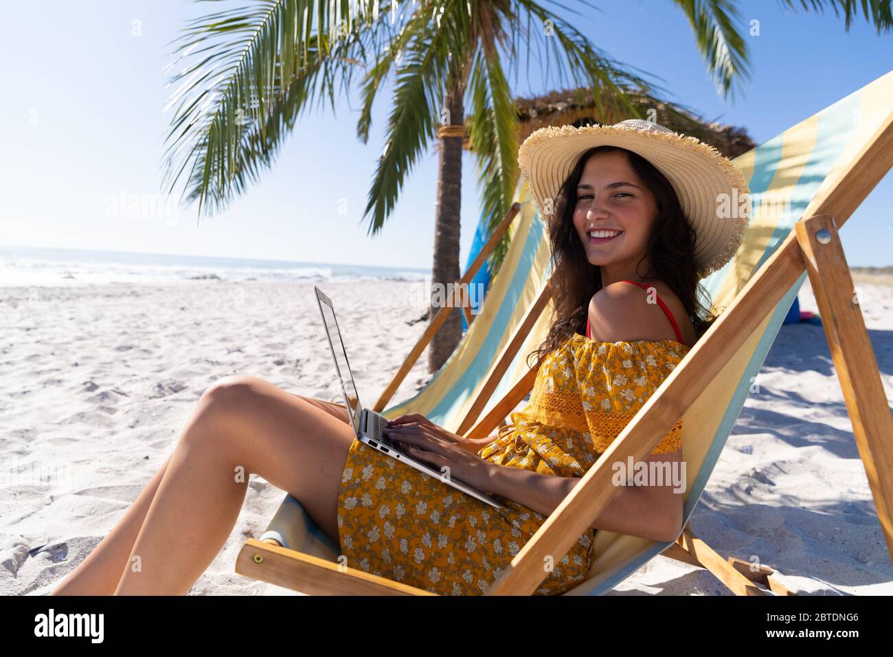 Femme caucasienne assise sur une chaise longue et utilisant un ordinateur portable à la plage Banque D'Images
