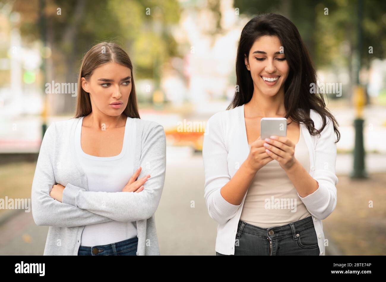 Jalouse fille regardant le téléphone de l'ami marcher ensemble à l'extérieur Banque D'Images