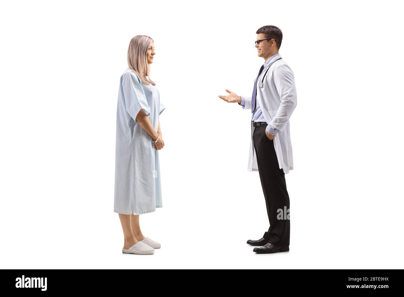 Photo de profil d'un médecin de sexe masculin parlant à une jeune femme dans une robe de patient isolée sur fond blanc Banque D'Images