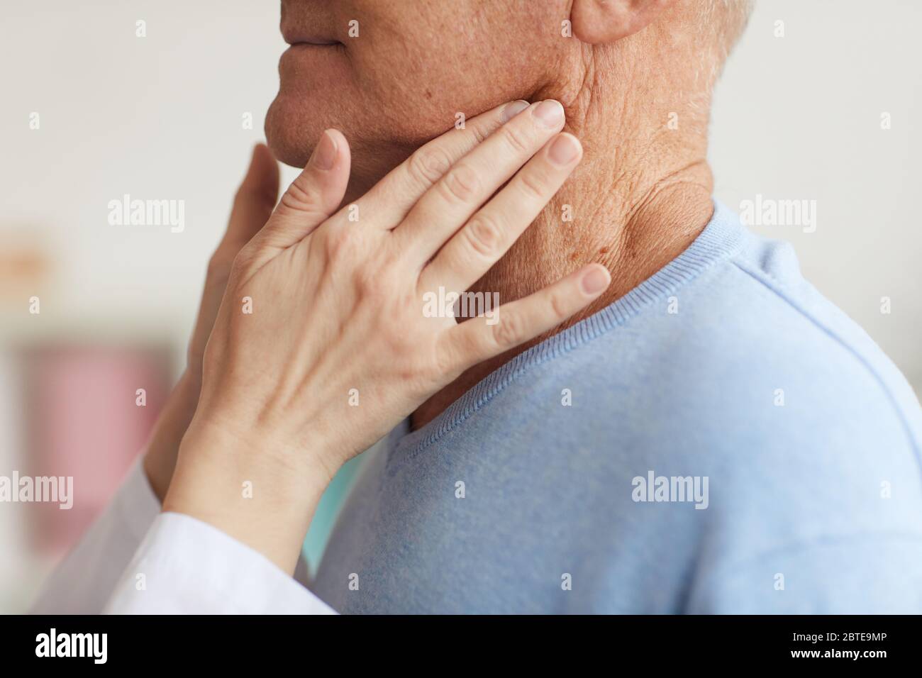 Gros plan d'une femme méconnue qui palpse le cou d'un patient âgé tout en l'examinant lors d'une consultation en clinique Banque D'Images