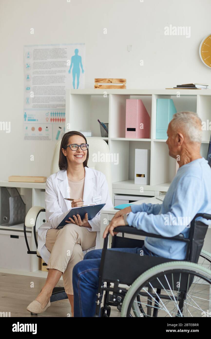 Portrait d'une femme souriante médecin consultant un homme âgé handicapé en fauteuil roulant pendant la consultation en clinique Banque D'Images
