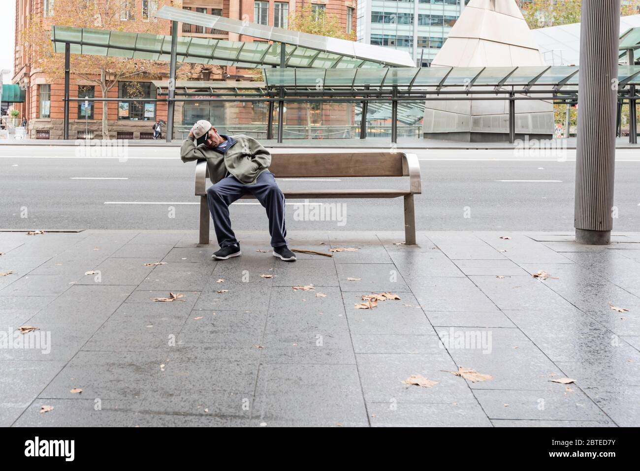 Un homme, sans abri, dort pendant la journée sur un siège en bordure de trottoir à côté de six voies de circulation près de la gare centrale de Sydney, en Australie Banque D'Images
