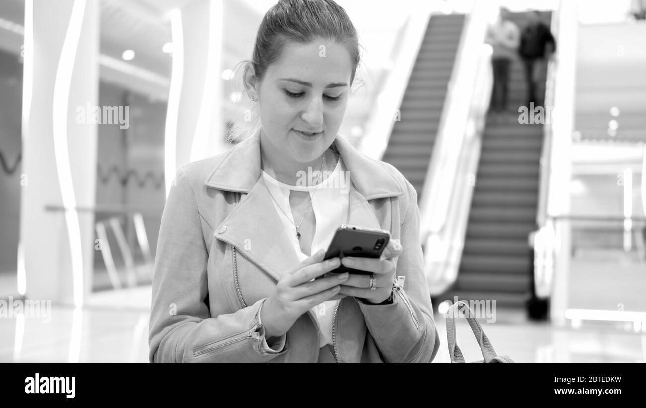 Portrait noir et blanc de la belle jeune femme dans le centre commercial qui navigue sur Internet sur un smartphone Banque D'Images