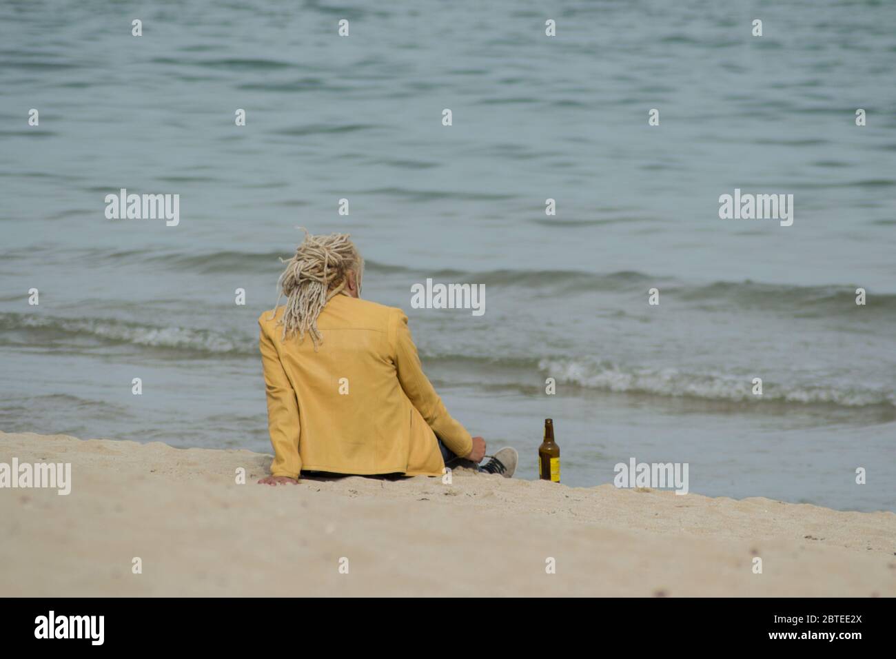 Homme blond avec des dreadlocks sur la tête, buvant de la bière et se relaxant près de l'eau sur la plage Banque D'Images