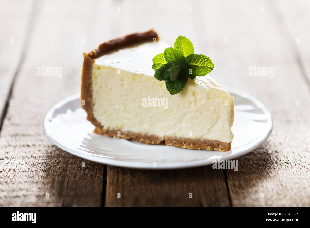 Tranche de cheesecake New York classique avec une branche de menthe sur une plaque sur une table en bois. Le concept de la boulangerie et des desserts aux gâteaux sucrés Banque D'Images