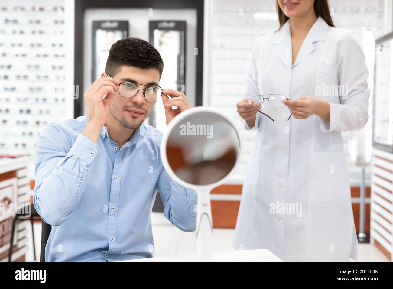 Spécialiste aidant un jeune homme à choisir des lunettes Banque D'Images