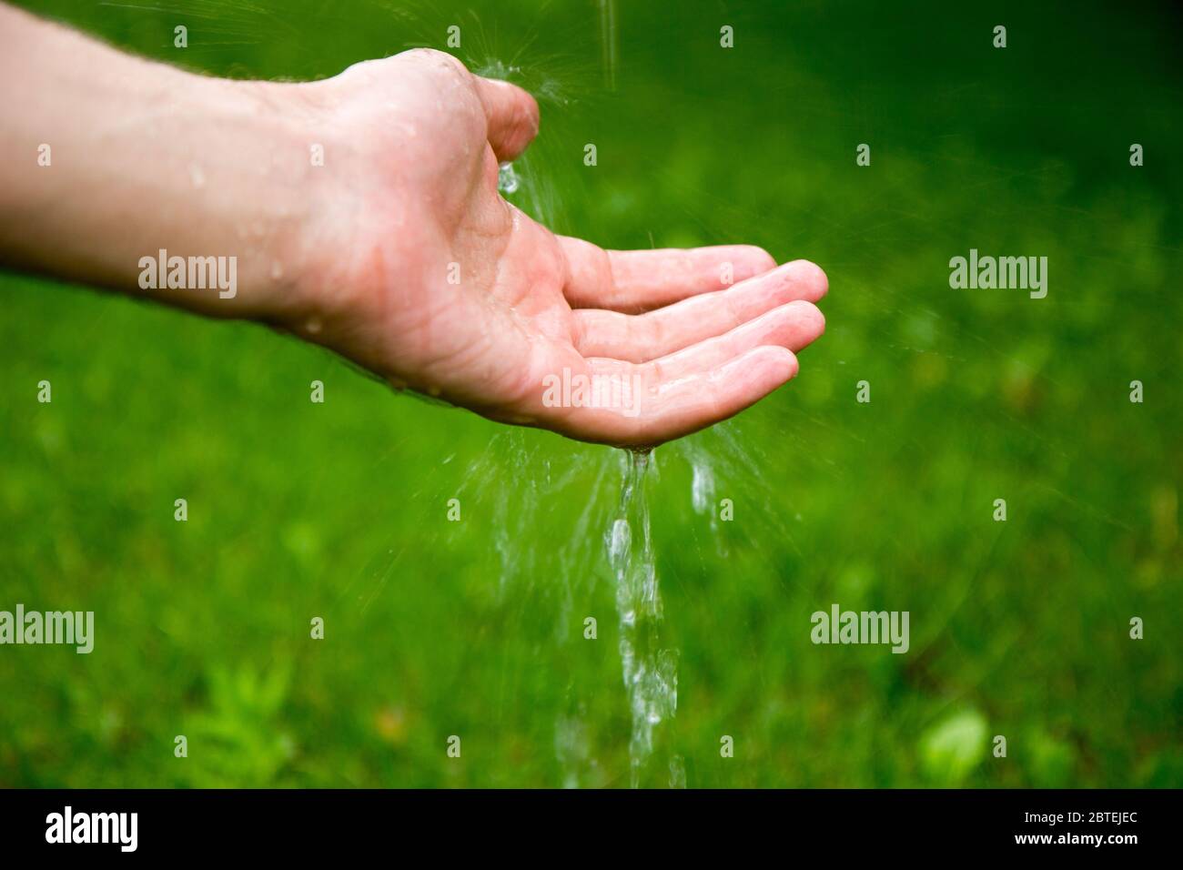 Eau qui coule sur une main sur un fond vert (pelouse). Banque D'Images