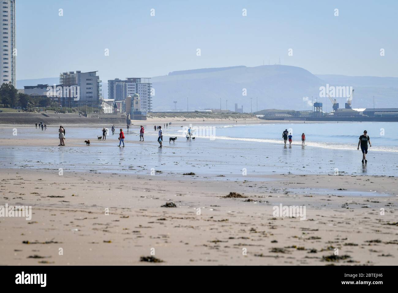 Les gens marchent le long de la plage par temps chaud à Swansea, au pays de Galles, où des restrictions de confinement restent en place pour lutter contre la propagation du coronavirus. Banque D'Images