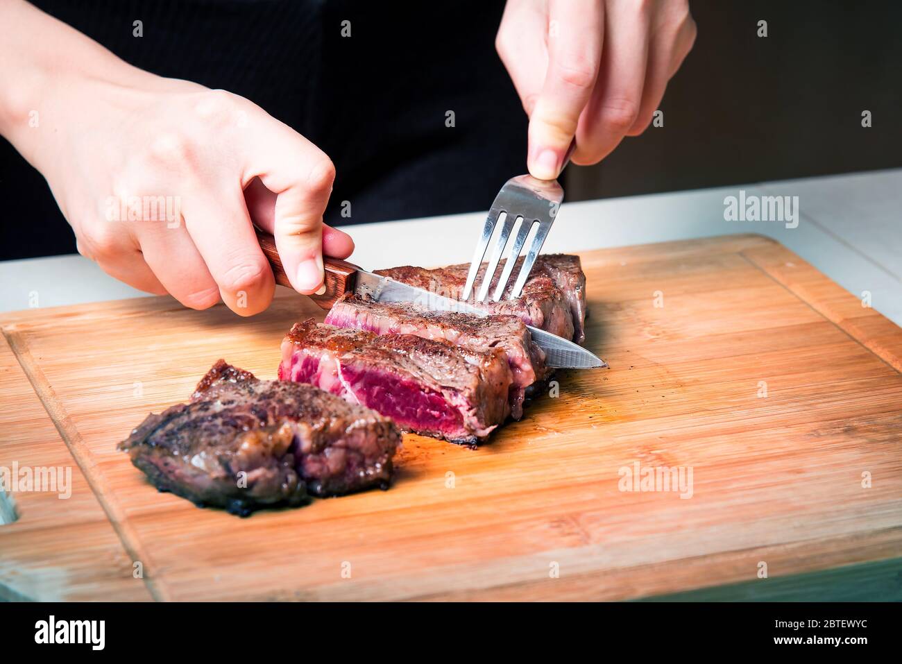 Femme coupant du steak de bœuf pendant la friture à bord. Préparation de nourriture à domicile Banque D'Images