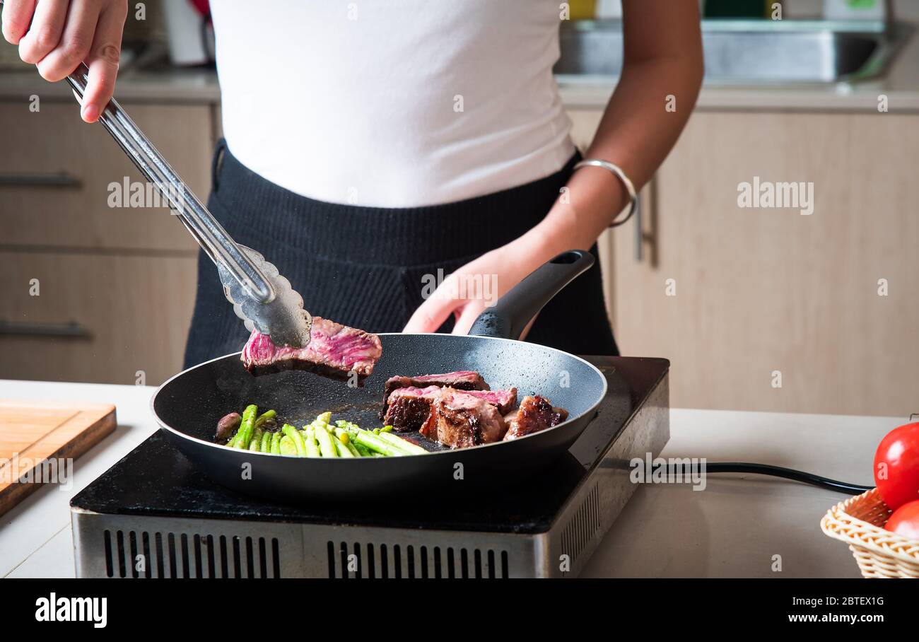 Femme friture de steak de boeuf avec bébé asperges sur la poêle. Préparation de nourriture à domicile Banque D'Images