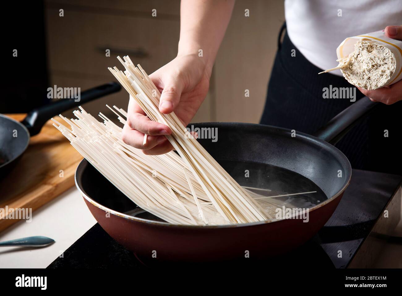 Femme cuisant des nouilles dans la cuisine. Préparation de nourriture à domicile Banque D'Images