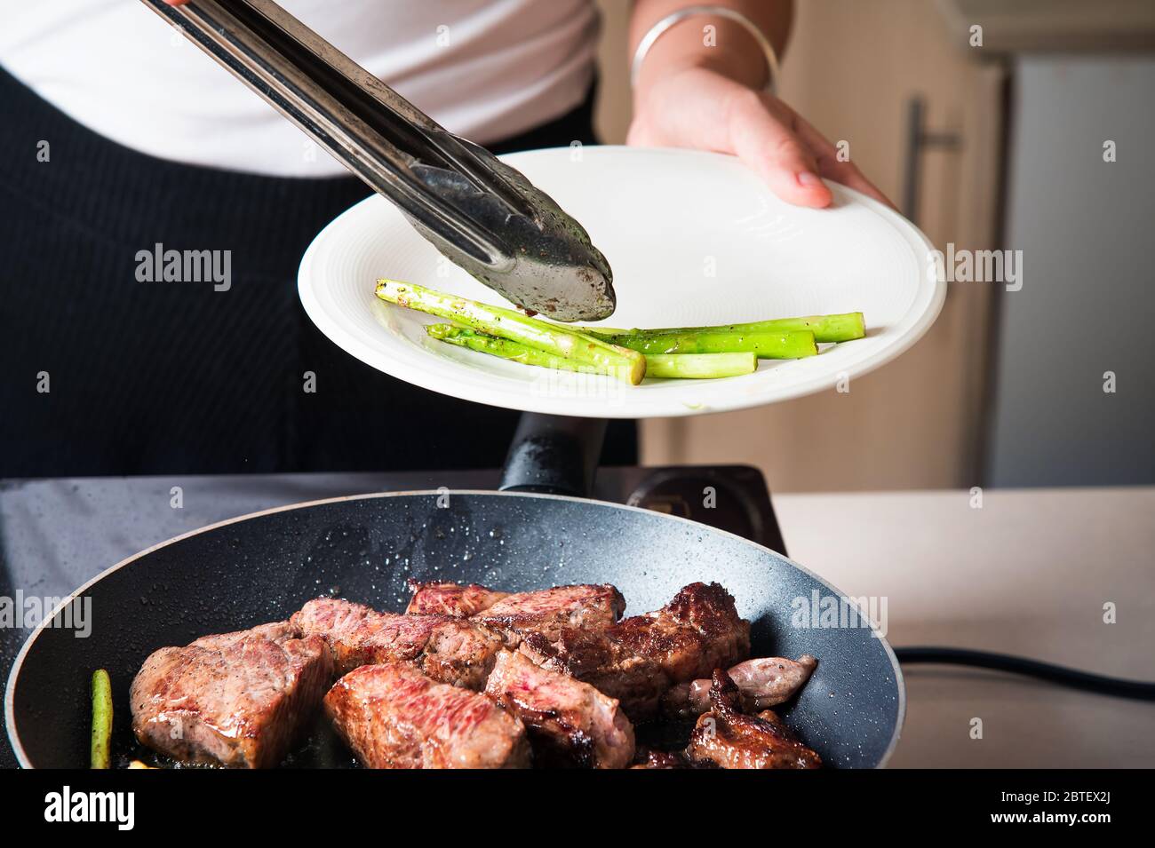 Femme servant un steak de bœuf avec des asperges de bébé sur la poêle. Préparation de nourriture à domicile Banque D'Images