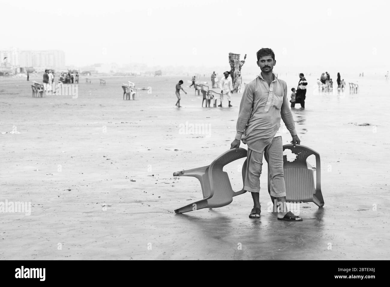 Homme debout sur la plage tenant des chaises à Clifton, Karachi, Pakistan 29/06/2012 Banque D'Images