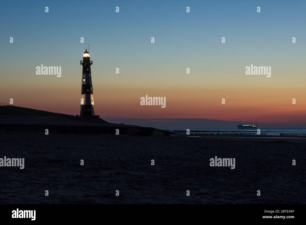 Plage de la mer du Nord au crépuscule avec le phare Nieuwe Sluis et le bateau qui navigue au loin Banque D'Images