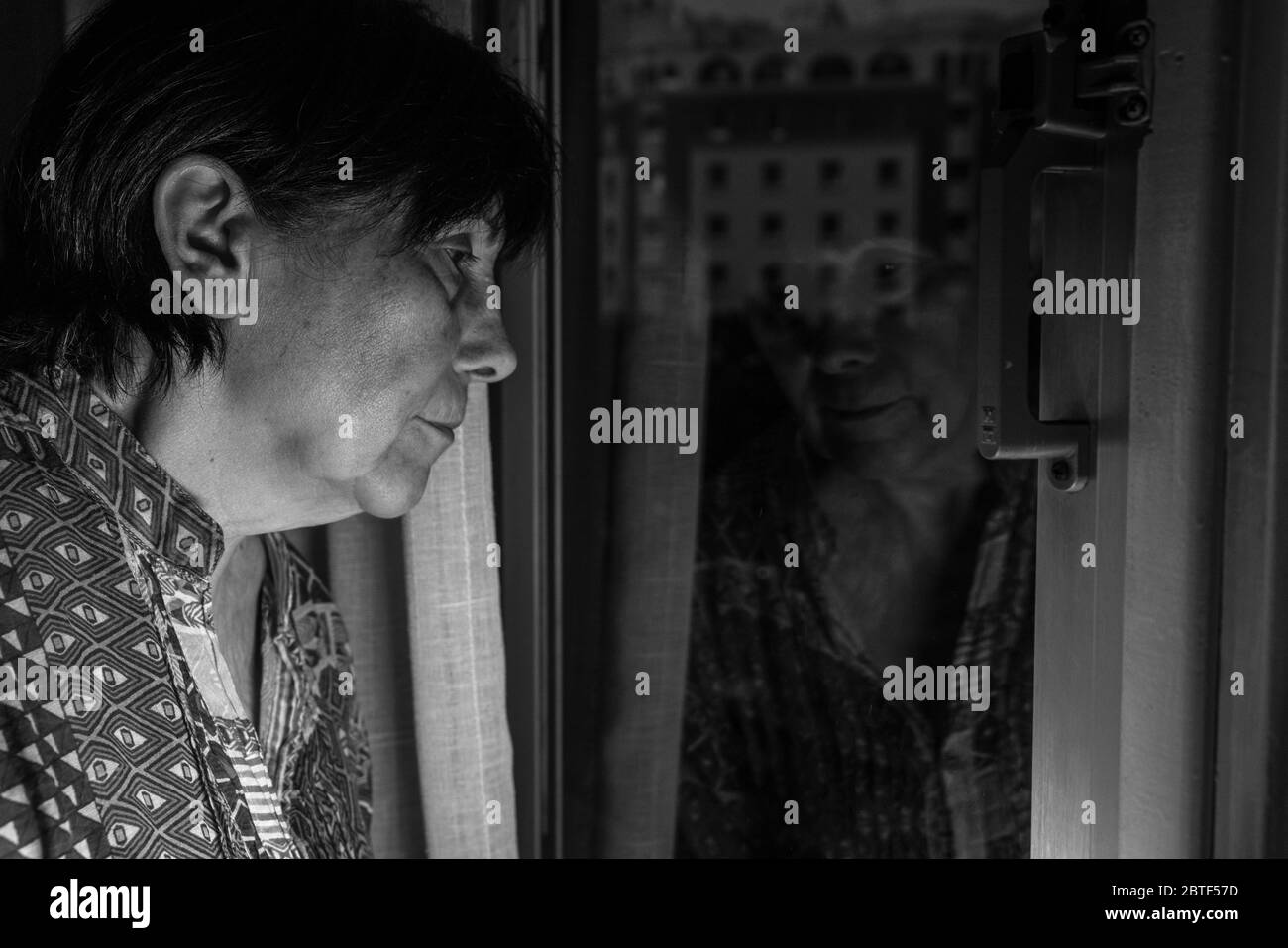 Image artistique noir et blanc triste avec la vieille femme fermer la fenêtre en temps de virus corona. Barcelone, Espagne. Banque D'Images