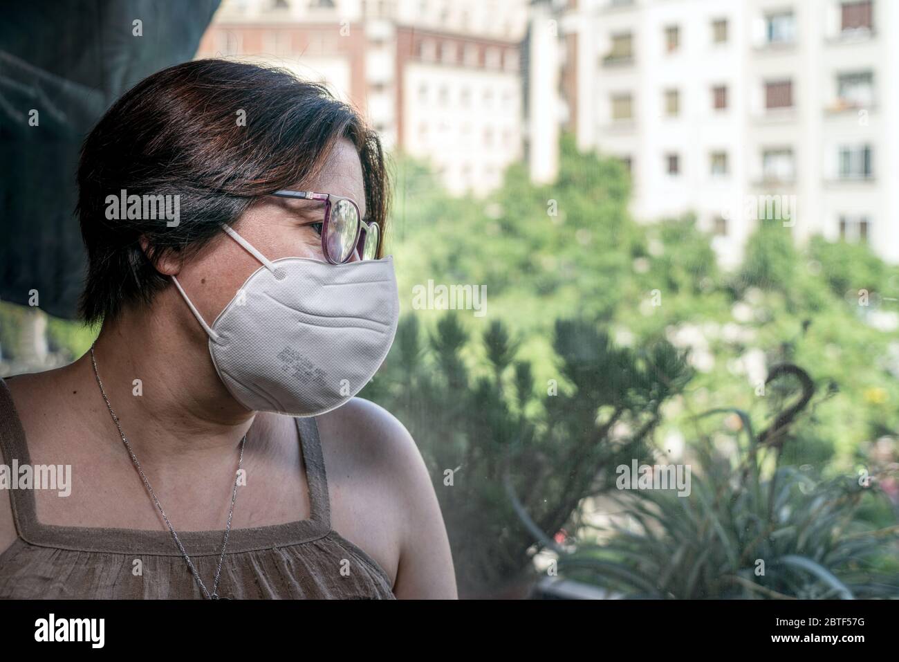 Femme regardant à travers la fenêtre avec masque facial. Barcelone, Espagne. Banque D'Images