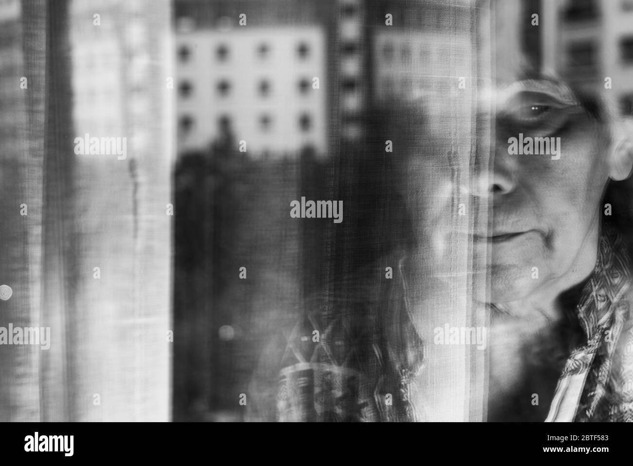Image triste en noir et blanc avec la vieille femme fermer la fenêtre en temps de virus corona. Barcelone, Espagne. Banque D'Images