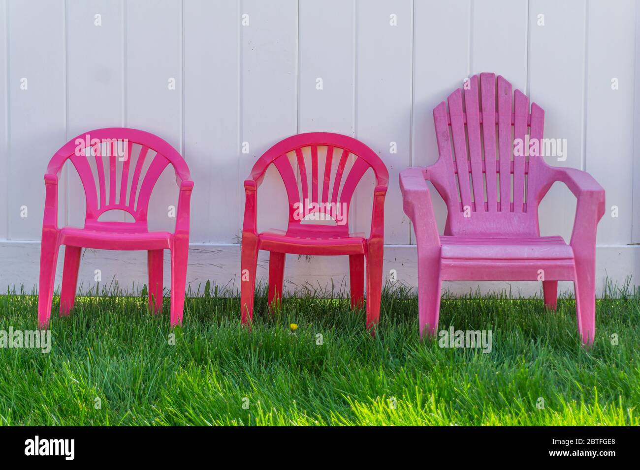 Trois chaises en plastique colorées pour enfants sur la pelouse, contre une clôture en bois blanc Banque D'Images