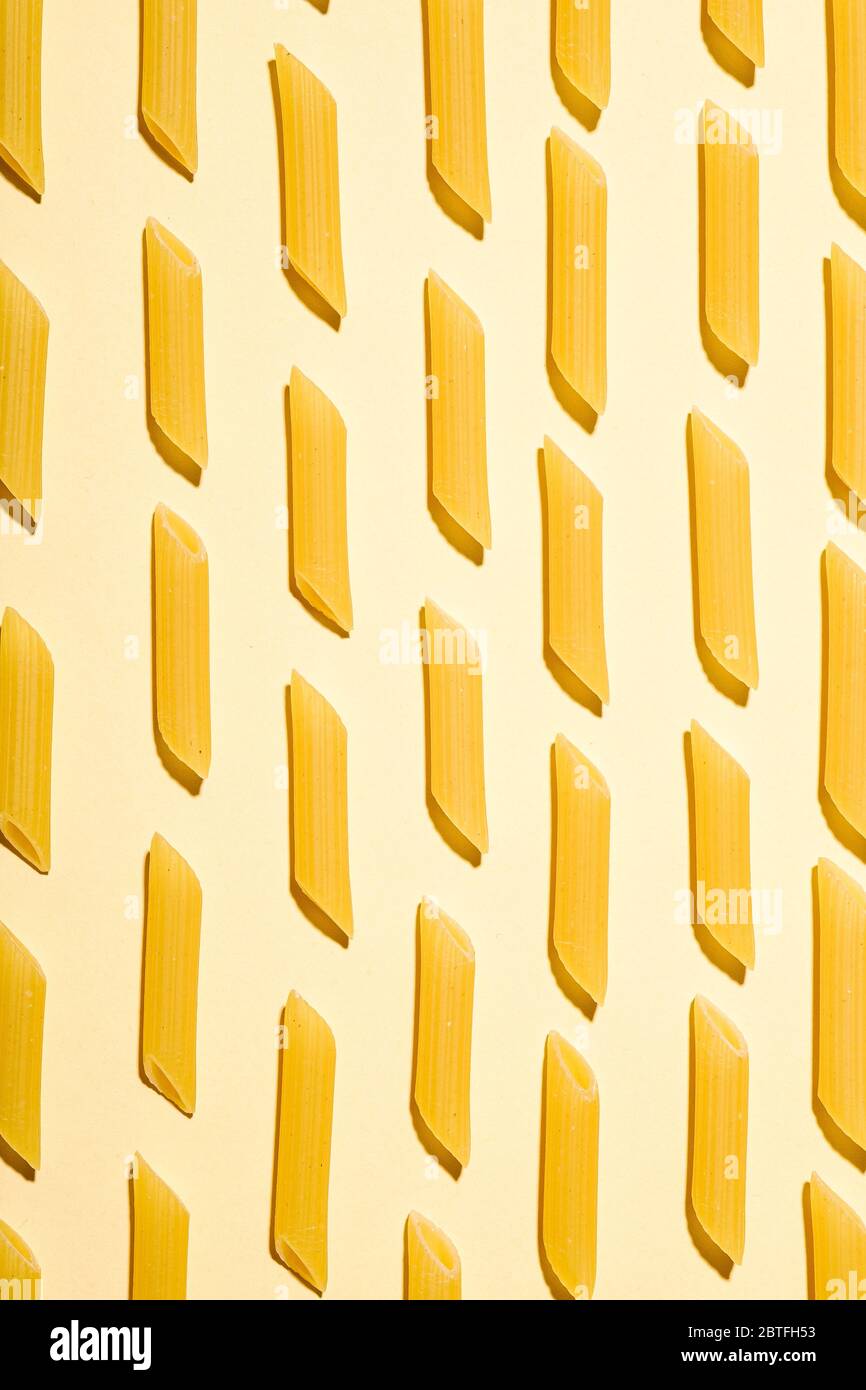 Pâtes italiennes, motif macaroni en tube de penne brut sur fond jaune crème, vue du dessus, nourriture abstraite Banque D'Images